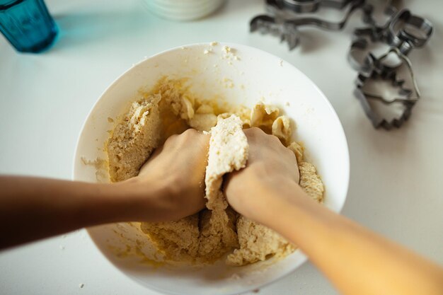 Foto l'adolescente di mani si siede al tavolo e impasta la pasta per cuocere i biscotti in cucina a casa.