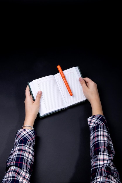 The hands of a teenager hold a notebook with a pen.