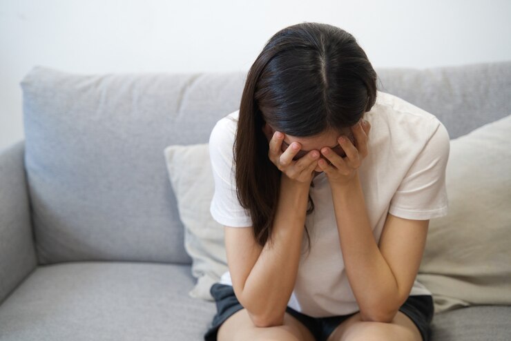ソファーに座っていた若い失望アジア女の子の寺院に手。