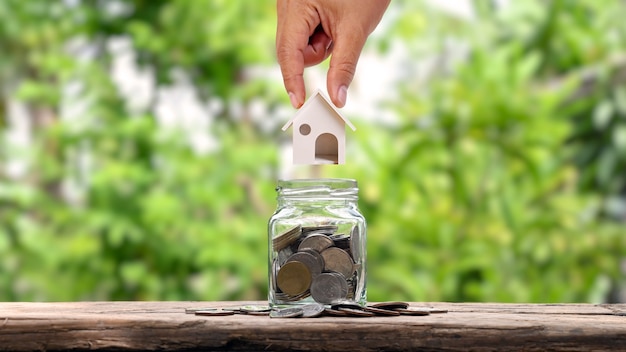 Hands that house models put in a jar for savings, money-saving ideas to buy a house.