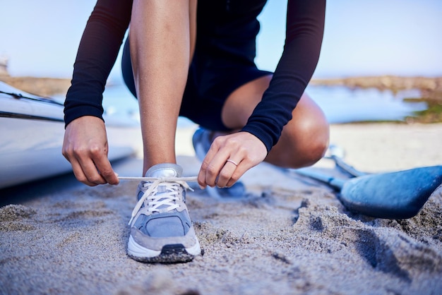 Hands tie shoes beach and athlete start workout training and kayak exercise outdoor Sand person and tying sneakers at ocean to prepare in fitness sports and healthy body for wellness in summer