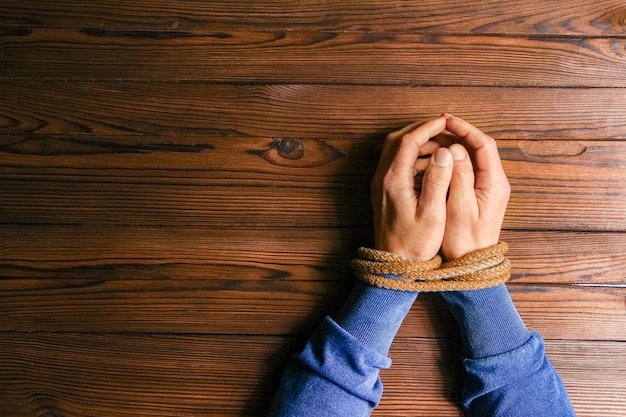 Hands tied with a rope life-threatening on a wooden background.