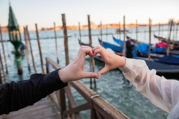 Hands of two lovers make a heart shape in Venice gondolas in the background concept of romance and love