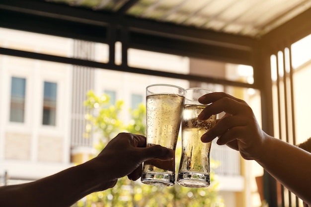 The hands of two men holding a glass of beer raised together to drink to celebrate the success