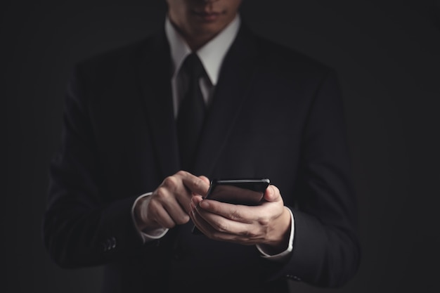 hands typing message on smart phone. Handsome businessman in black suit.