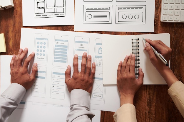 Hands of ui and ux designers working with wireframes and layouts of mobile application view from above