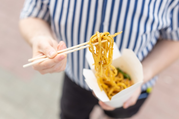 Hands of an unidentified young man in a striped shirt holding a box of chinese noodles in the street