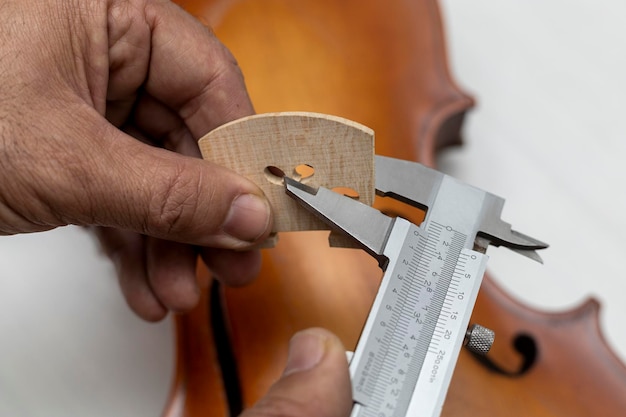 Hands of an unrecognizable latin american luthier taking\
precise measurements of a violin bridge with a vernier concept\
stringed instruments