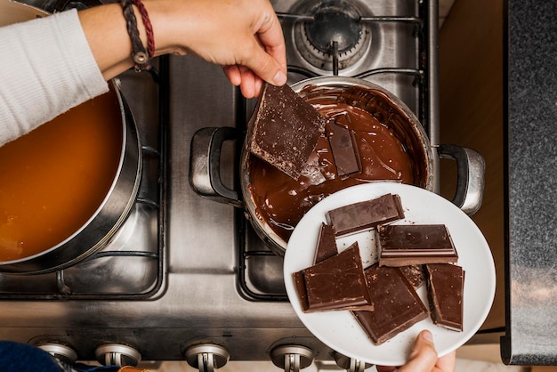 Hands of an unrecognizable person putting pieces of solid chocolate in pot to prepare chocolate sauce for the preparation of the homemade Argentine alfajores recipe