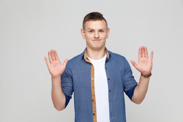 Hands up young boy wearing white tshirt and blue shirt looking at camera and give up