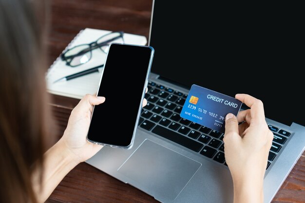 Hands using a mobile phone while holding a credit card in front of the computer