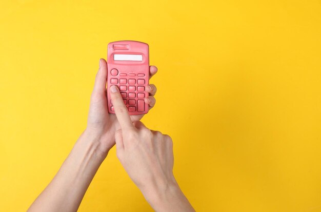 Photo hands using pink calculator on yellow background minimalism