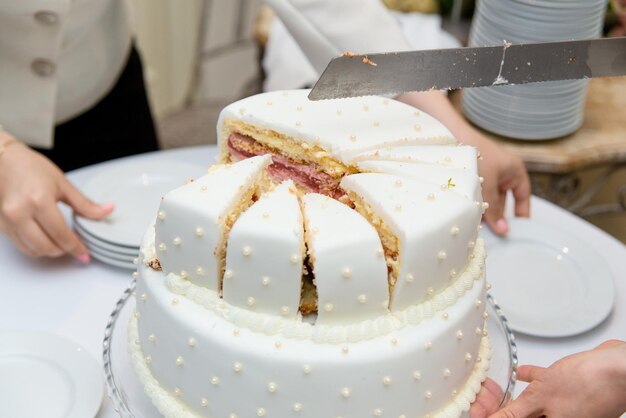 Mani di un cameriere che tagliano la torta nuziale