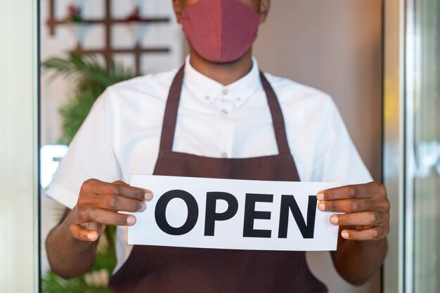 Photo hands of waiter in uniform and protective mask holding paper with notice open by transparent door of cafe or restaurant before working day