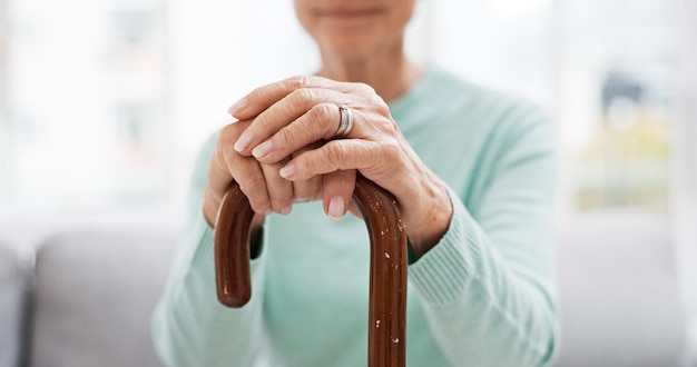 Hands walking stick and elderly woman with walking stick on a sofa for balance support and mobility Walk aid and old female at senior care facility with disability dementia or chronic arthritis