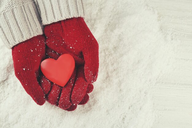 雪の背景に心を保持している暖かい赤い手袋の手