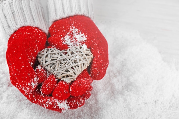雪の背景に籐の心を保持している暖かい赤い手袋の手