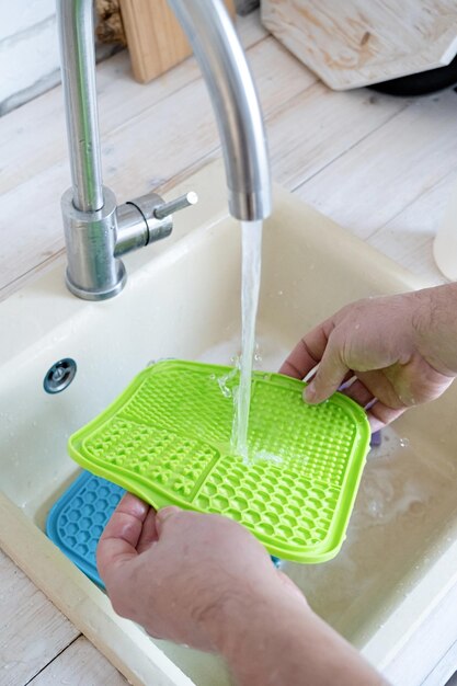 hands washing pet lick mat in kitchen sink