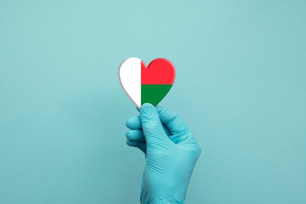 Hands wearing protective surgical gloves holding madagascar flag heart