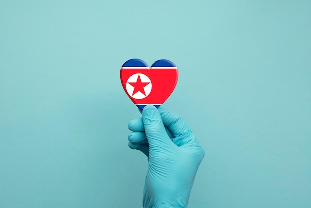 Hands wearing protective surgical gloves holding north korea flag heart