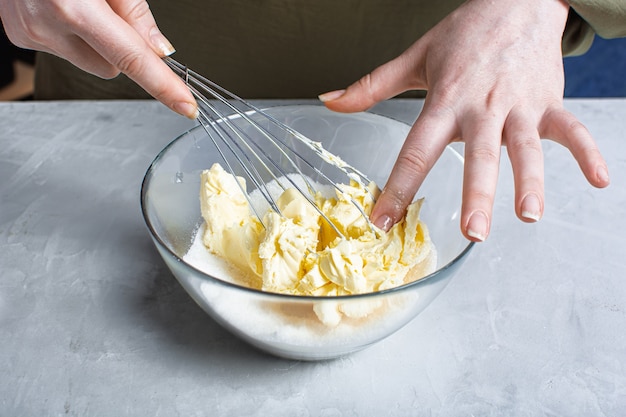 Hands whisk butter and sugar in a glass bowl