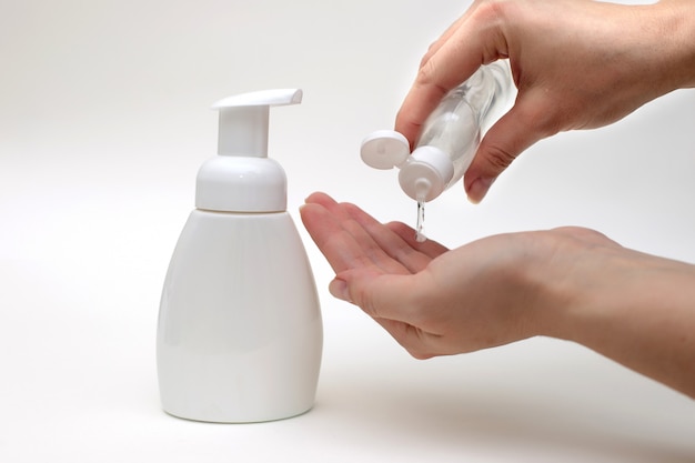 Hands on a white background are holding a bottle of antiseptic gel.