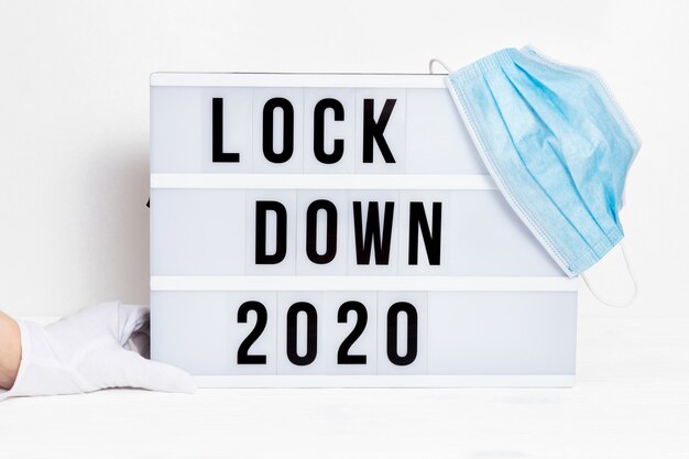 Hands in white gloves hold Light box with message lockdown 2020 and Surgical protective mask.