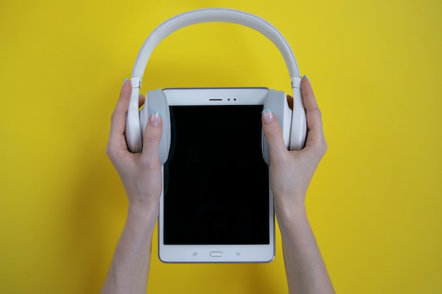 in hands white headphones are put on a white tablet on a yellow background