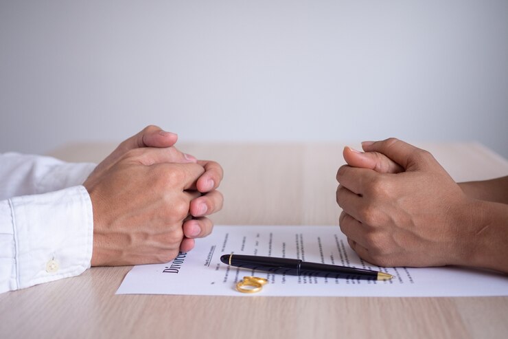 फोटो the hands of the wife and husband rests on the divorce documents. filing divorce documents or prenuptial agreements prepared by a lawyer. the wedding ring represents the covenant of lovers.