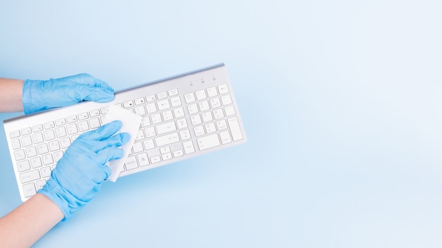 hands with blue medical gloves cleaning a keyboard with disinfectant