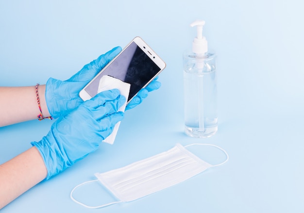 hands with blue medical gloves cleaning a phone with disinfectant