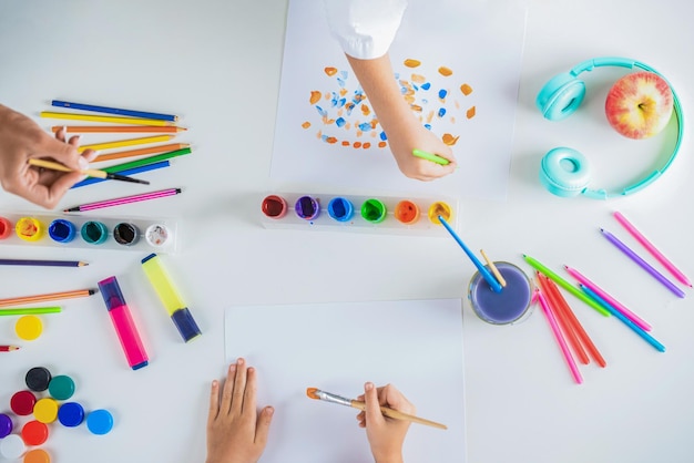 Hands with brush painting with watercolor abstract stains Hands paint brush Kid hands painting at the table with art supplies Drawing on a white sheet of paper Creativity and art