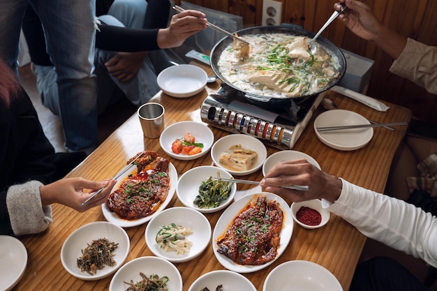 Hands with chopsticks clamping korean food and boiled tofu soup on wooden table