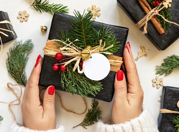 Руки с рождественским подарком с круглым пустым подарочным ярлыком с еловыми ветвями и декором Мокет