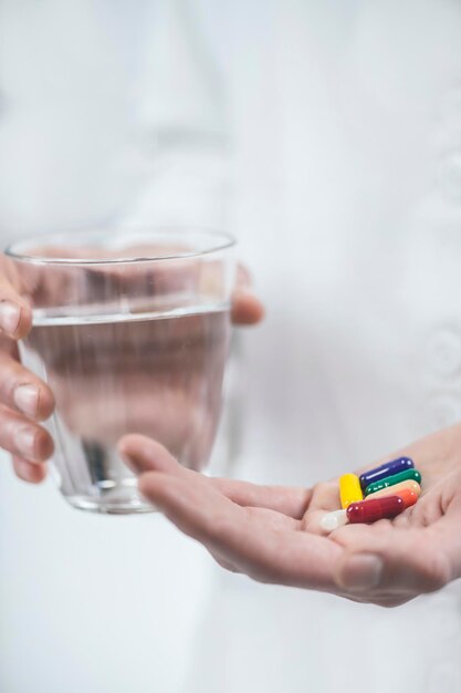 Foto mani con pillole colorate e un bicchiere d'acqua