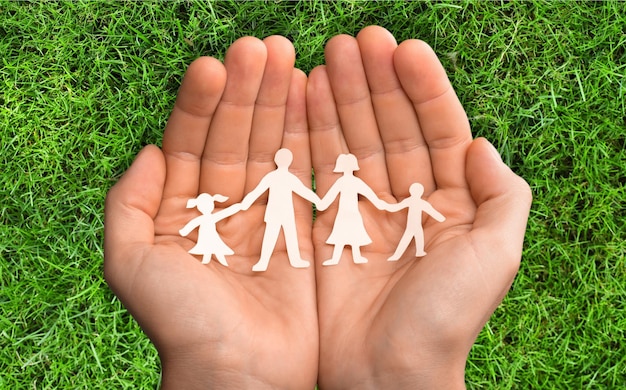 Hands with family of paper people on park background