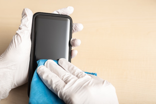 Hands with gloves cleaning mobile phone with disinfectant. COVID-19 Coronavirus prevention concept.