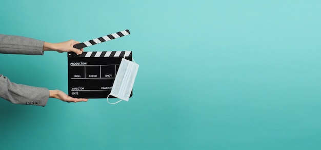 Hands with grey suit and hold black Clapper board or movie slate with face mask. it use in video production ,movies and cinema industry on blue and green or mint background.