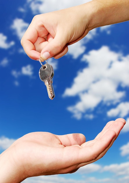 Hands with key on a background sky