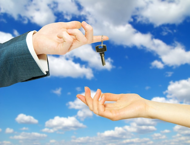 Hands with key on a background sky