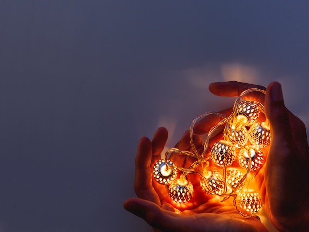 Hands with light bulbs in shape of heart. Metal light bulbs with delicate pattern shine in dark. 