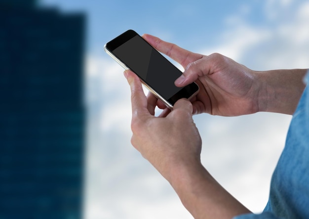 Mani con il telefono contro il cielo e l'edificio sfocato