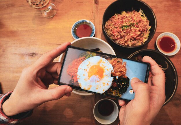 Photo hands with the phone takes picture of korean food with fried egg