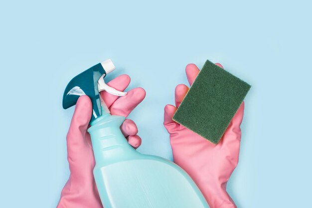 Hands with pink rubber gloves holding a cleaning sponge and a cleaning product sprayer