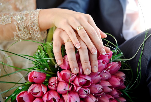 Mani con anelli sposa e sposo sul bouquet da sposa di rosa