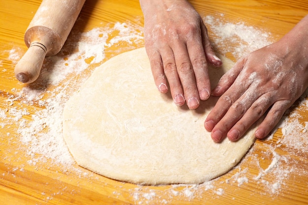 Hands with rollingpin make dough for pizza Italian pizza cooking preparation process on wood table