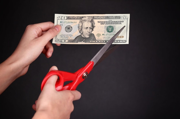 Hands with scissors cutting dollar banknote on black background