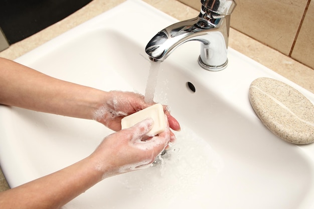 A Hands with soap are washed under the tap with water