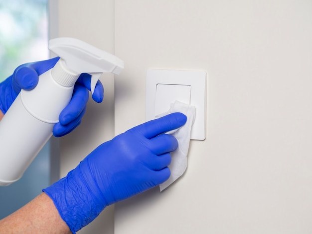 Photo hands with surgical gloves cleaning light switch