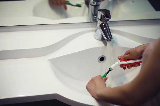 Hands with tooth brush and paste on blurred background in the\
bathroom in the sink selective focus